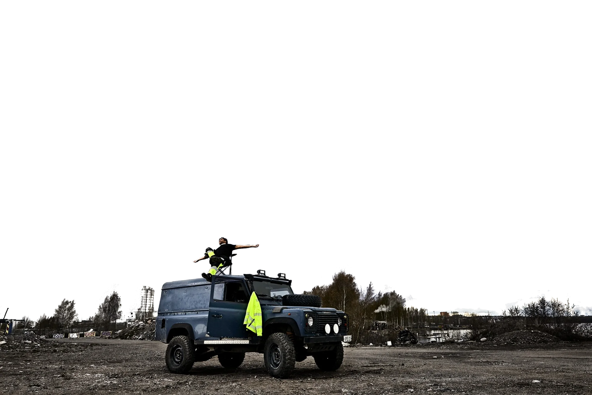 Man in Dimex hi-vis trousers stretching his arms wide on the roof of a Land Rover under a stormy sky